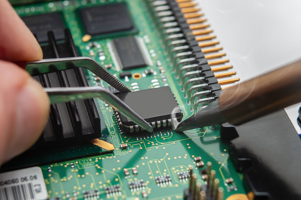 The repairer is soldering an IC in a PLCC package to the circuit board of an electronic device